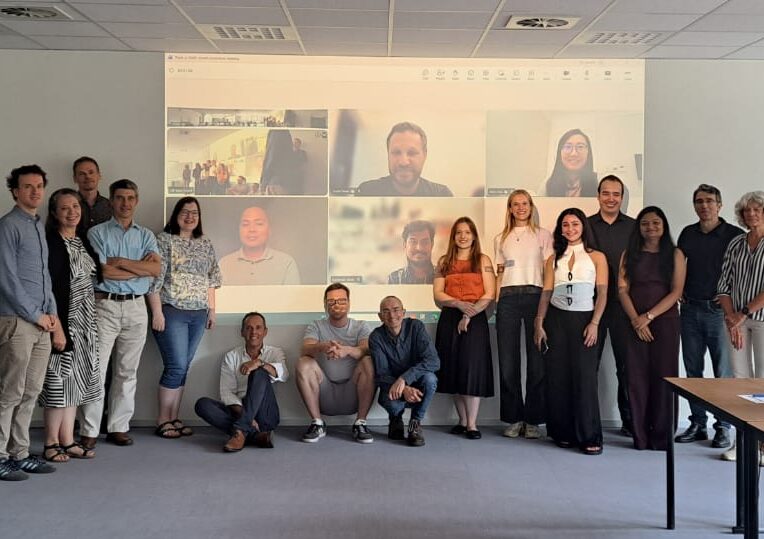 Group photo of Triple-A-COAT partners in the meeting room in front of screen with online participants